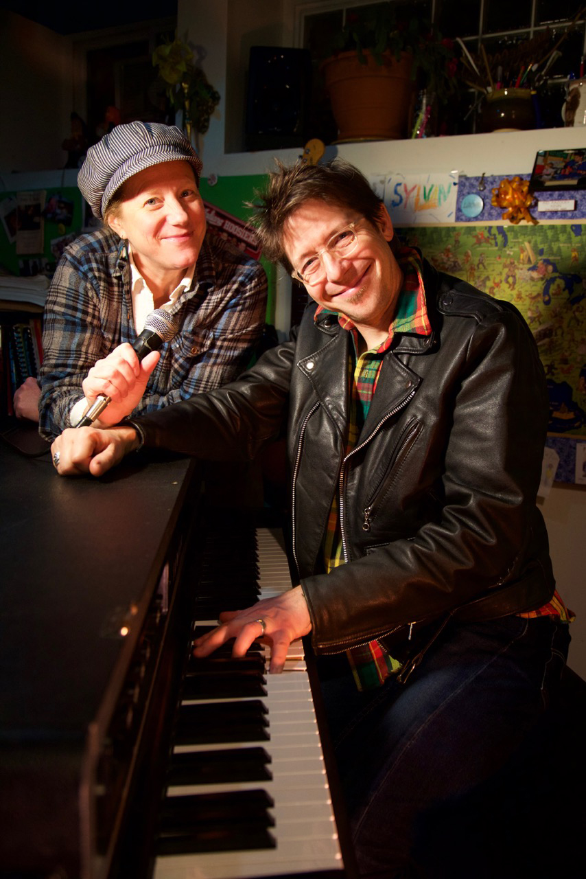 A man and woman stand around a piano