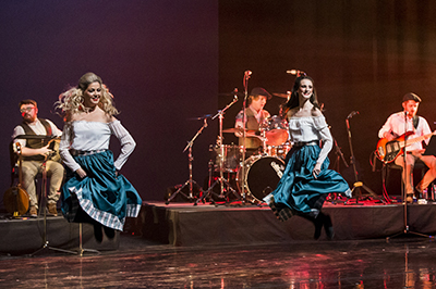 Dancers in green dresses perform onstage with several musicians.