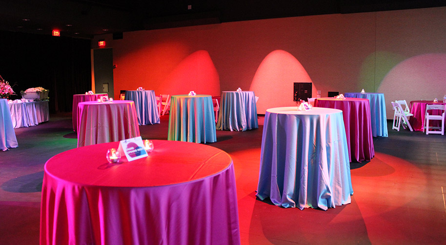 A chic social event in the Studio Theater with seating removed. Cocktail tables are aglow in pink and amber lighting.