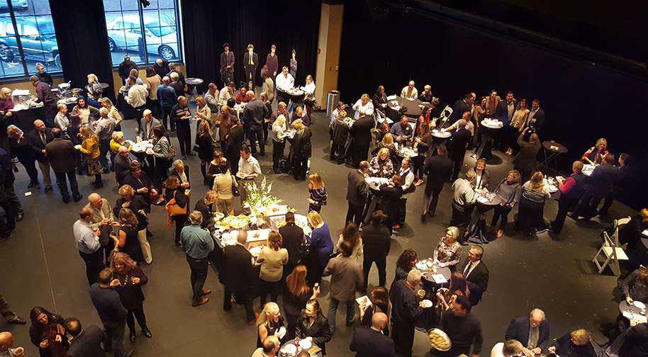 People mingling at an event in the Studio Theater. Seating has been removed to make room for cocktail tables and a buffet.