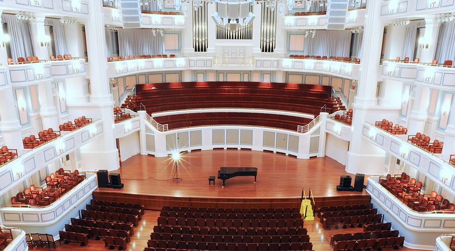 A piano and ghost light sit on the Palladium stage while the concert hall is empty.