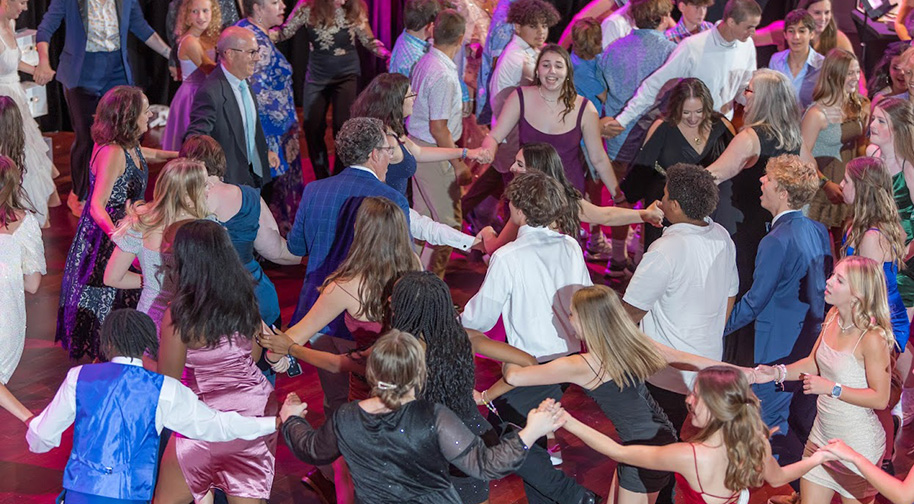 Party attendees dance in a circle holding hands on the Palladium stage.