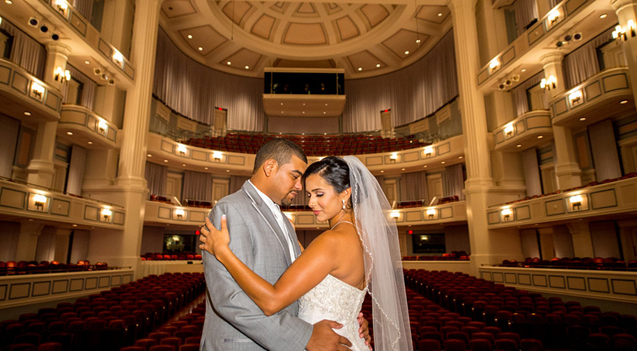 A bride and groom pose for a warmly lit photo on the Palladium stage.