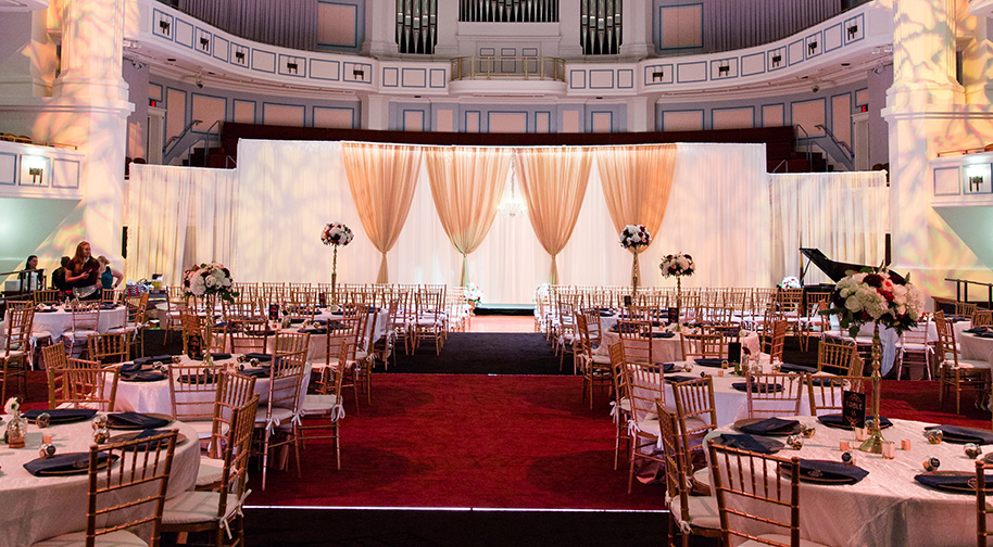 A wedding reception is set with tables and a dance floor in the Palladium concert hall.