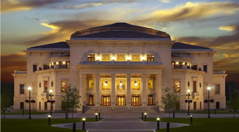 A large limestone building, the Palladium, is lit up at dusk with dramatic clouds in a blue sky.