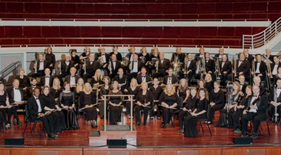 Seated in black dresses and tuxedos, members of the Indiana Wind Symphony pose onstage at the Palladium concert hall.