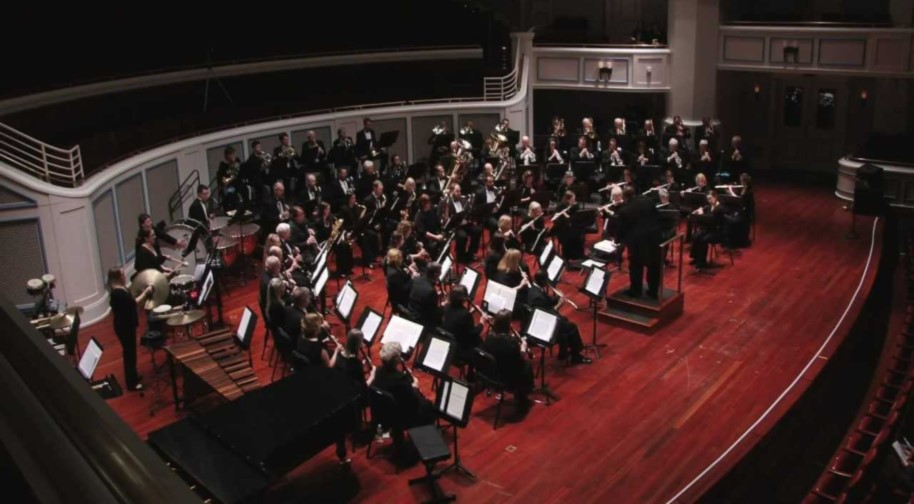 Seated in black dresses and tuxedos, members of the Indiana Wind Symphony perform onstage at the Palladium concert hall.