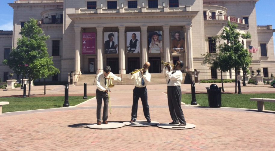 Statues of three jazz musicians stand outside the Palladium, a large neoclassical limestone building.