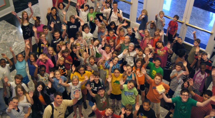 A large group of kids in the Palladium's West lobby excitedly wave to the camera.