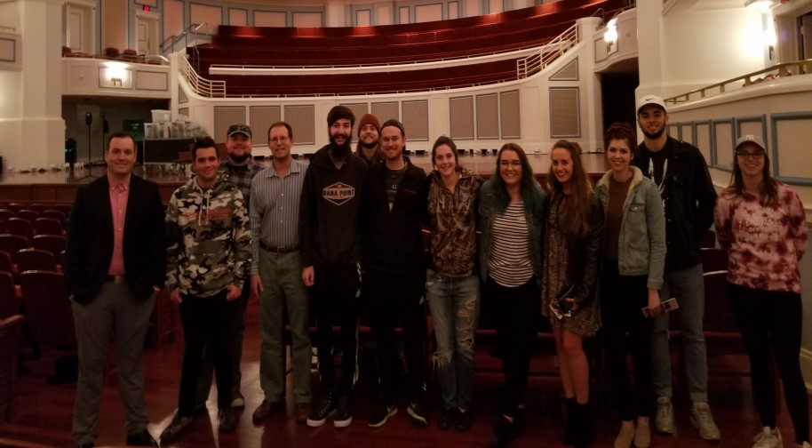 A group of young adults pose on the Palladium stage with Center for the Performing Arts staff after a tour.