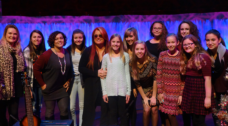 A group of thirteen women and girls of varying ages poses for a group shot on the Palladium stage.