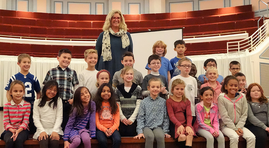 A class of students stands in rows for a posed photo on the Palladium stage with the teacher standing behind them.