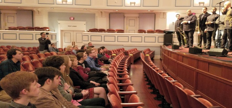 Young adult students sit in the third and fourth rows of the Palladium concert hall, leaning forward and listening intently to a band of musicians on stage who are speaking about their careers.