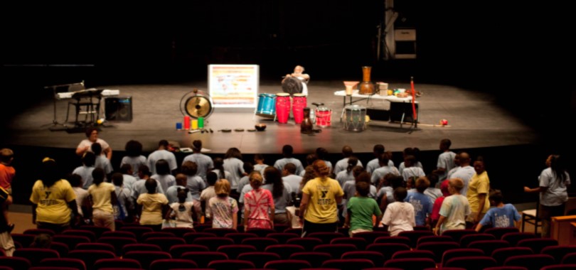 Viewed from behind, children watch a performer with instruments onstage at the Tarkington theater.