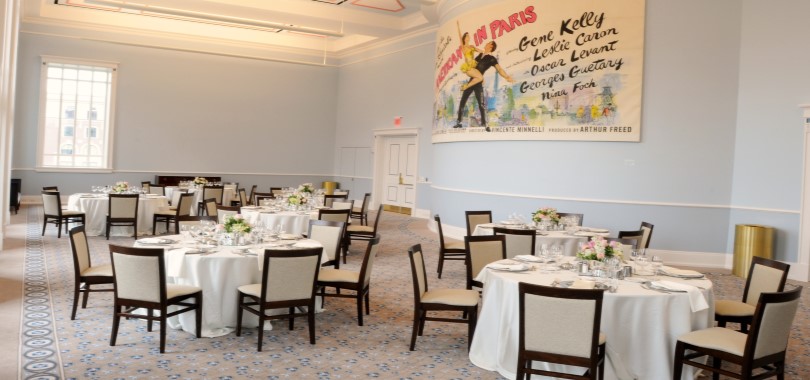 A large, carpeted gathering space with tables set for a meal and vintage movie billboard artwork on one wall.