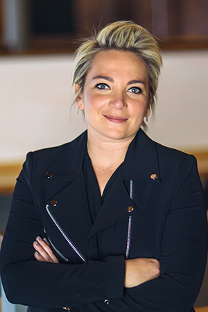 Keynote speaker Lindsay Boccardo, wearing a navy blue suit, stands smiling with arms crossed.