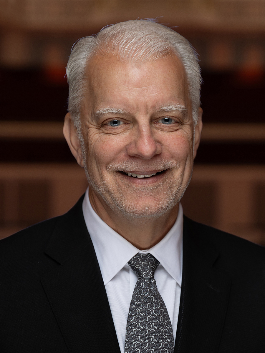 A man with white hair dressed in a dark suit and tie