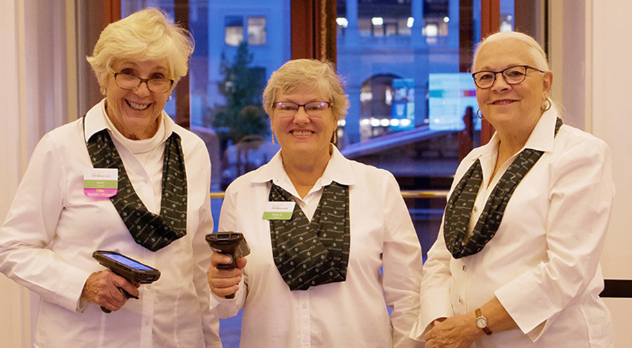 Three women in white uniforms with handheld ticket scanners smile while standing the Palladium lobby.