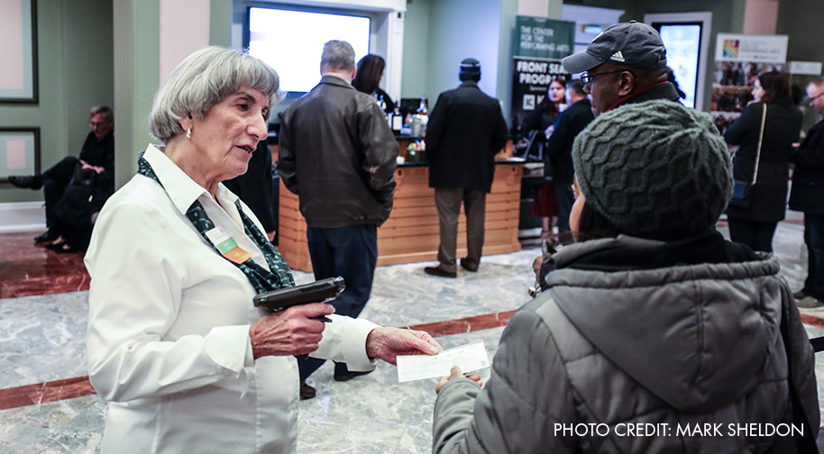 A uniformed female volunteer scans the ticket of a patron wearing winter clothes entering the Palladium's South Lobby. Photo by Mark Sheldon.