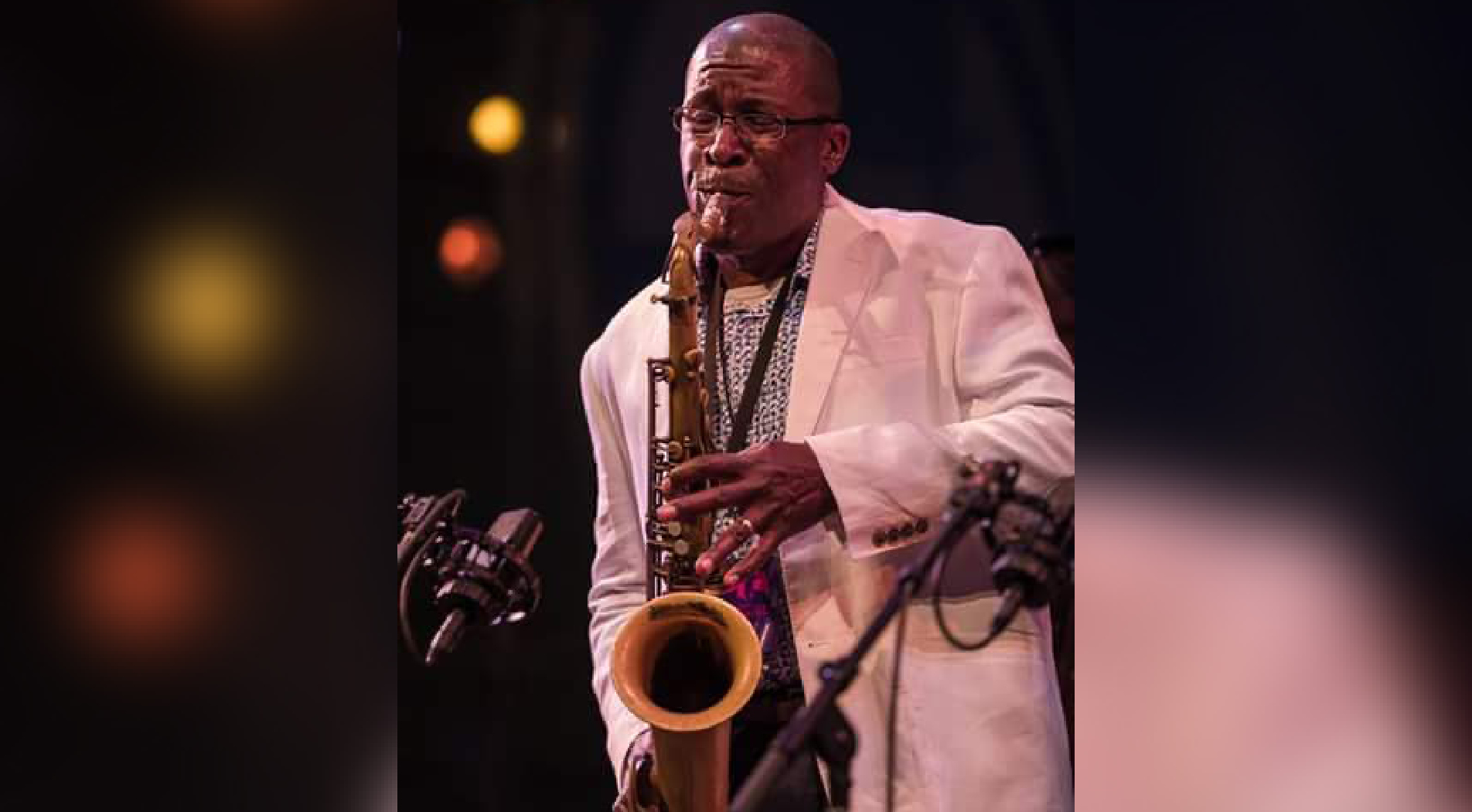 Man in a white suit coat plays the saxophone.