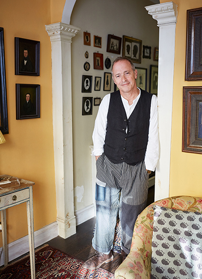 Author and humorist David Sedaris, a middle-aged man, poses in his home wearing casual clothes.