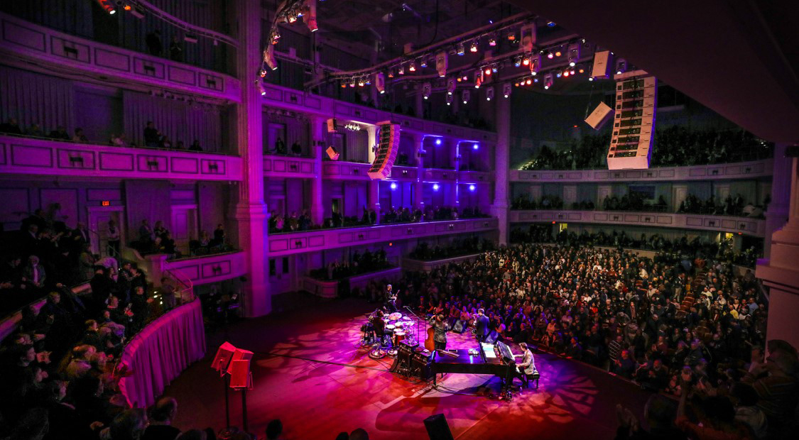 Trumpeter Chris Botti performs on the Palladium stage with a jazz combo. View from behind the stage to the right with a fishbowl effect showing a sold out crowd.