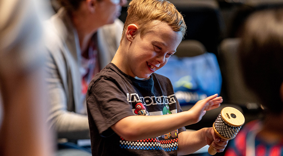 A young Prism Project camper smiles while playing a shaker instrument.