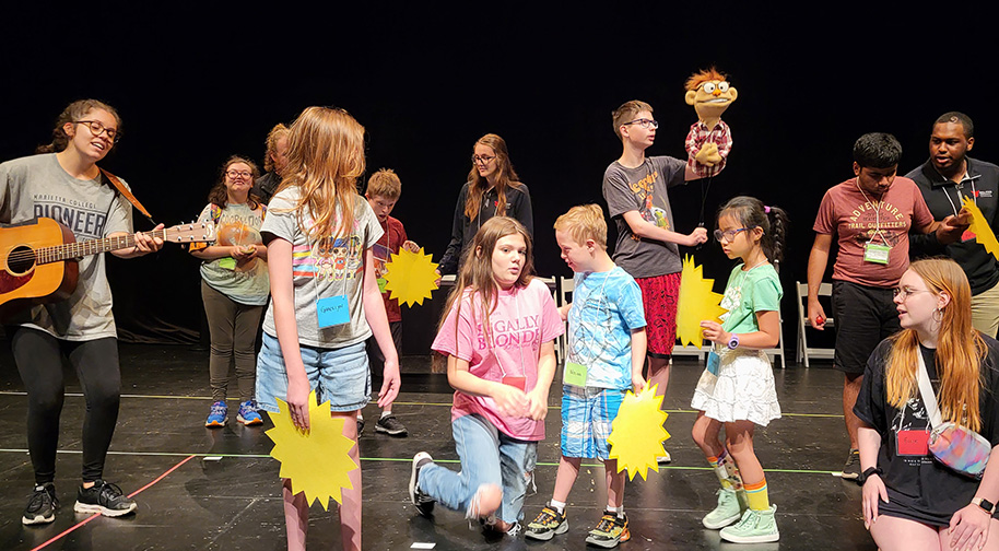 Prism Project campers of various ages rehearse a performance, all holding yellow star shapes.