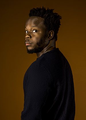 Trumpeter-composer Ambrose Akinmusire is dressed in black, looking back over his should at the camera.